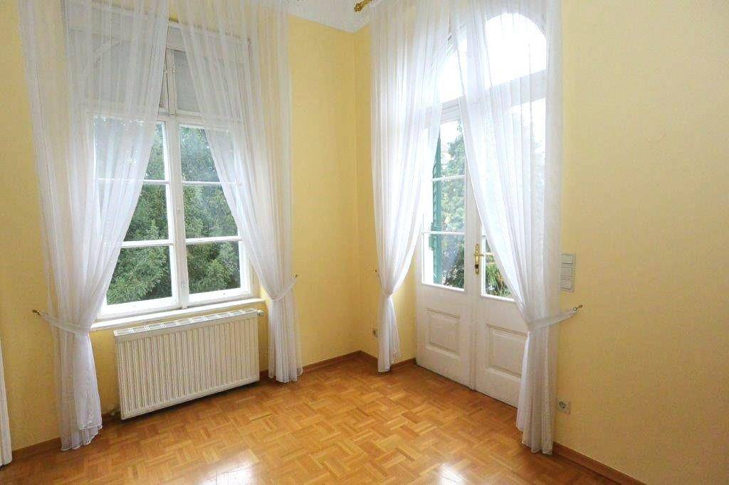 Sonniger Raum mit Parkettboden, gelben Wänden und Zugang zu einem französischen Balkon.