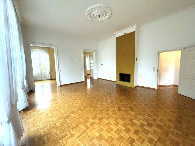 Großes Wohnzimmer mit Parkettboden, Kamin und dekorativer Deckenrosette, bereit zur individuellen Gestaltung.