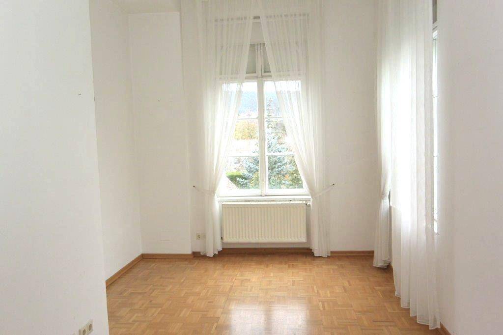 Helles Schlafzimmer mit Parkettboden und einem großen Fenster, das eine angenehme Atmosphäre schafft.