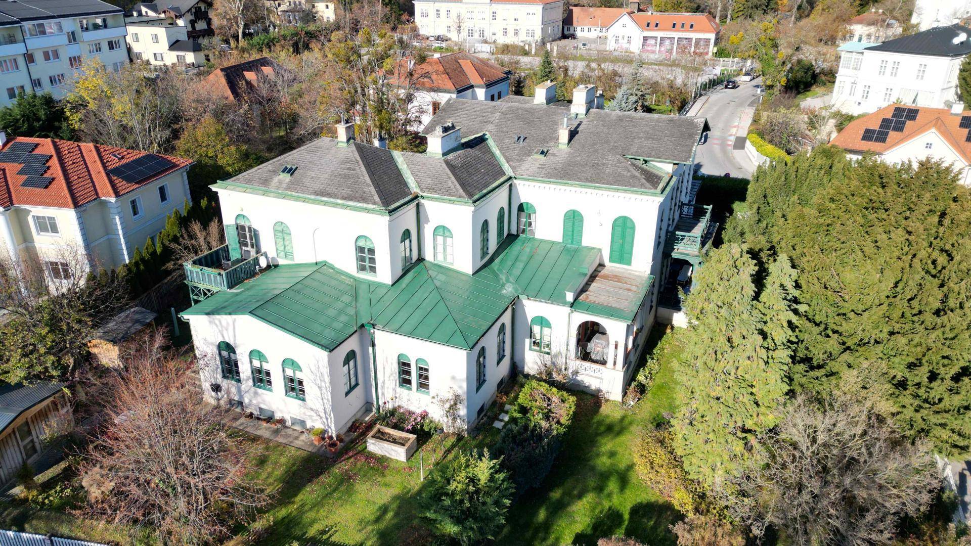Luftaufnahme der historischen Villa mit grünen Dächern, umgeben von einem großen Garten und weiteren Gebäuden.