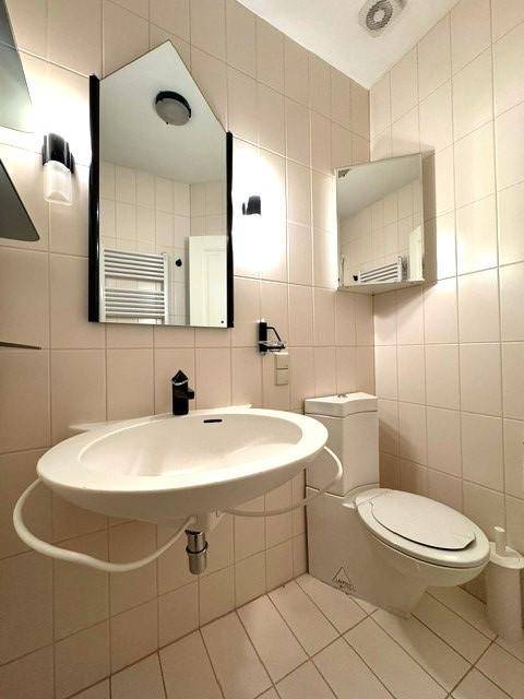 Gäste-WC mit Einzelwaschbecken, Toilette und Spiegelschrank, komplett gefliest.