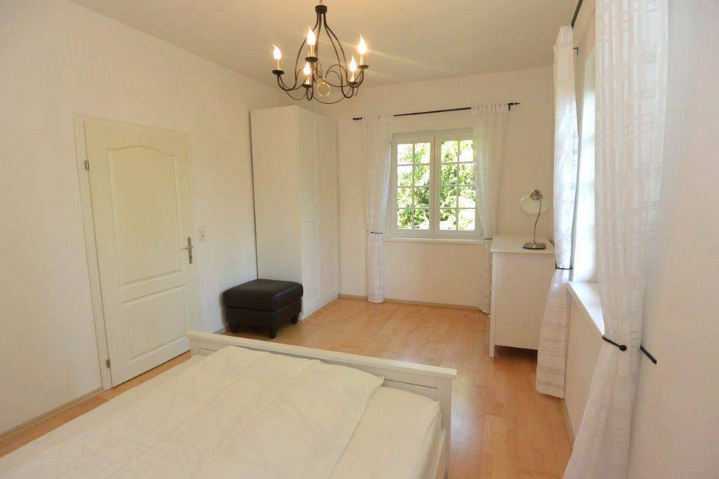 Gemütliches Schlafzimmer mit Holzboden, weißem Bett und Fenster mit Blick ins Grüne.
