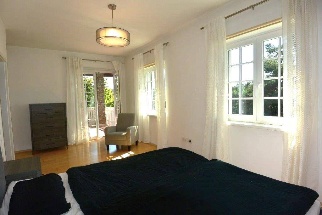 Helles Schlafzimmer mit Holzboden, Balkonzugang und Blick ins Grüne.