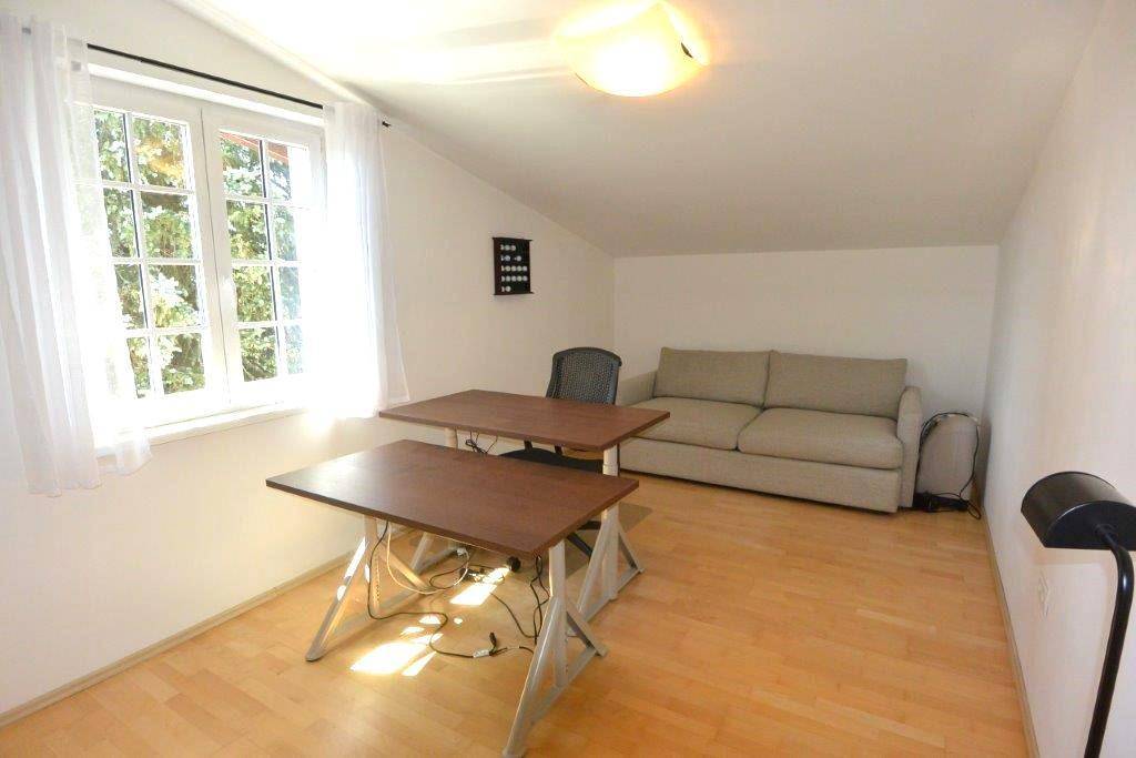 Helles Arbeitszimmer mit Holzboden, zwei Schreibtischen und einem Sofa.