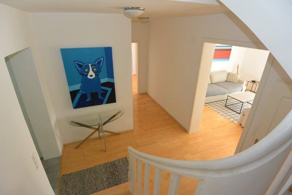 Heller Flur mit Holzboden, Treppenaufgang und farbenfrohem Kunstwerk.