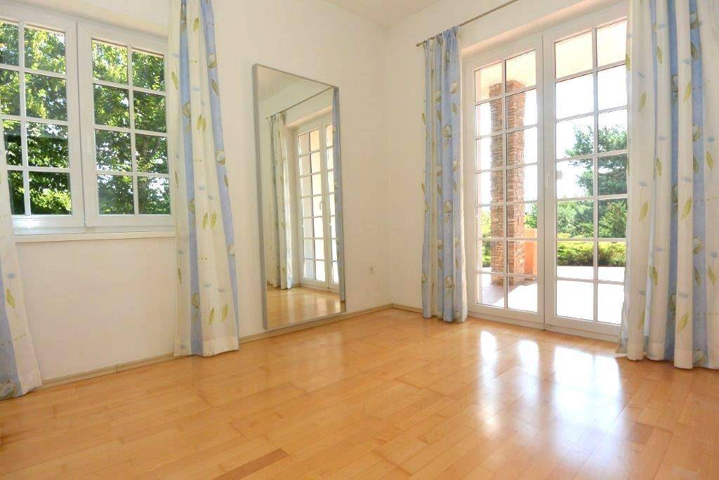 Heller leerer Raum mit Holzboden und großen Fenstertüren zum Außenbereich.