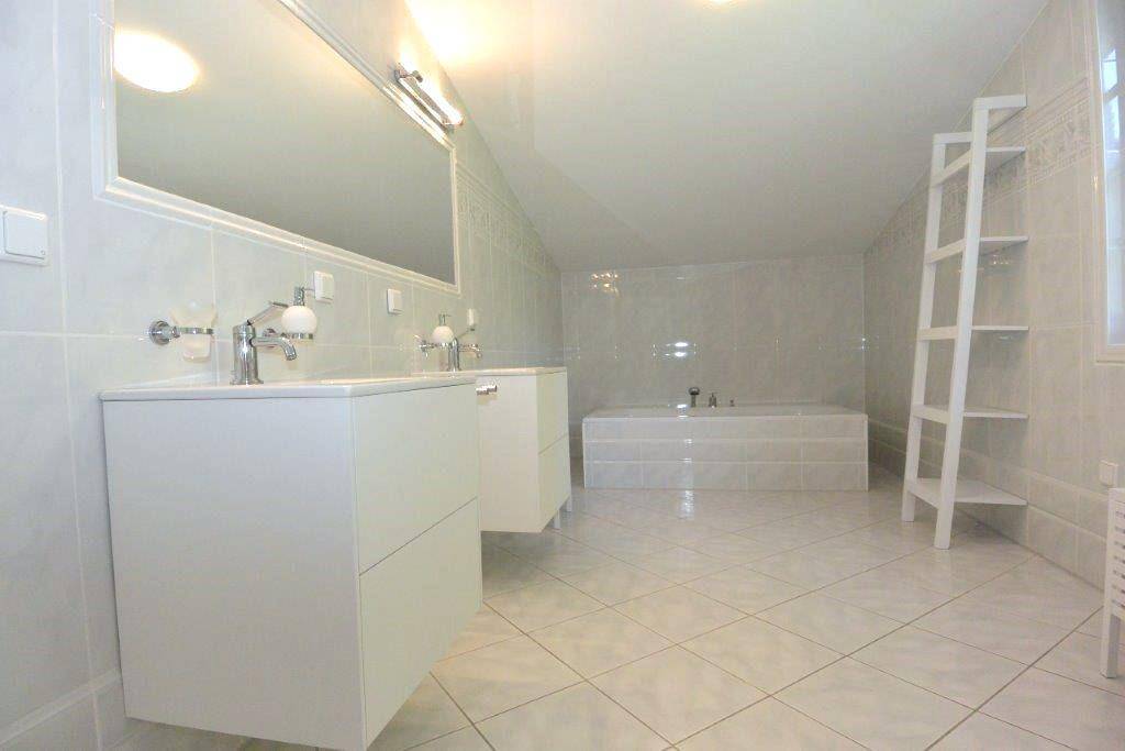 Helles Badezimmer mit Doppelwaschbecken, Badewanne und weißen Fliesen.