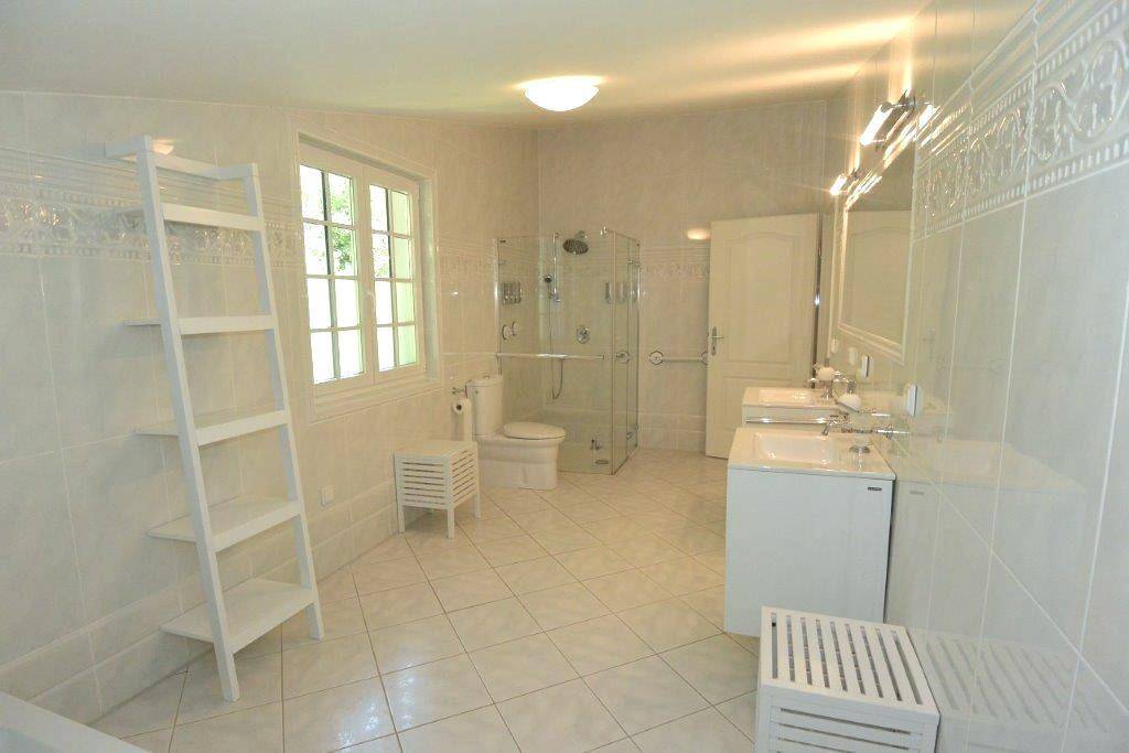 Geräumiges, hell gefliestes Badezimmer mit Dusche, WC und Fenster.