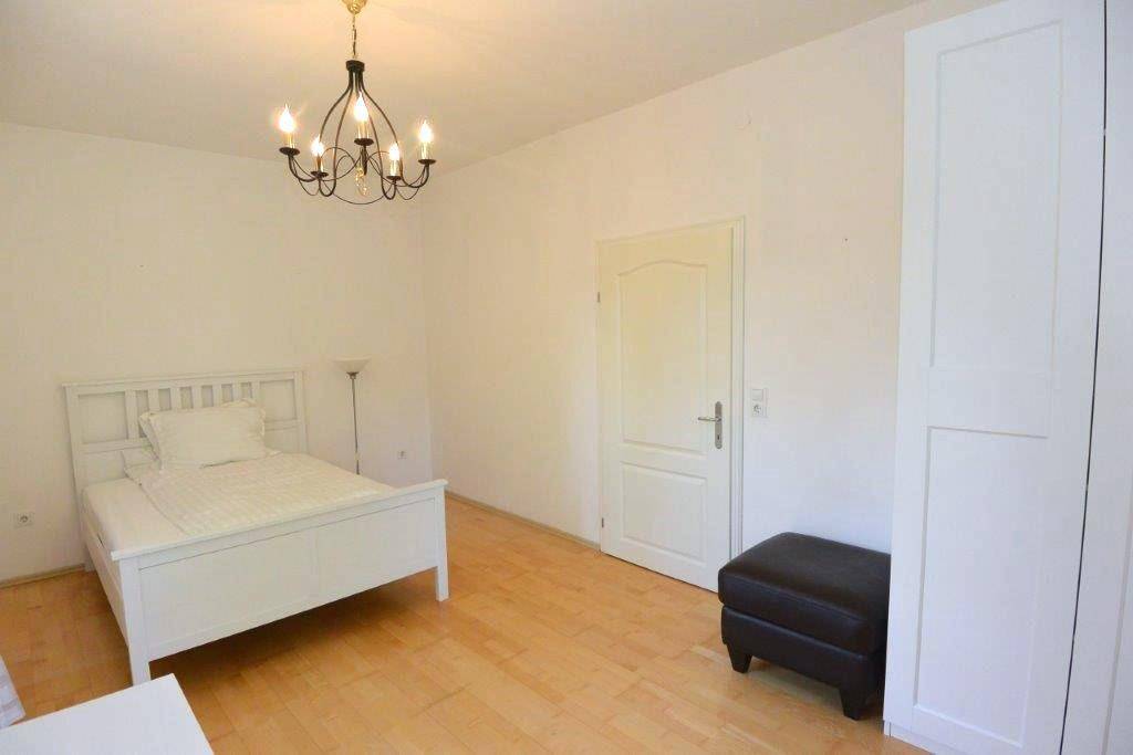 Helles Schlafzimmer mit Holzboden, weißem Bett und einem schwarzen Hocker.