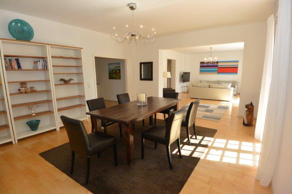 Geräumiger Essbereich mit Holzboden, großem Holztisch und Bücherregal.