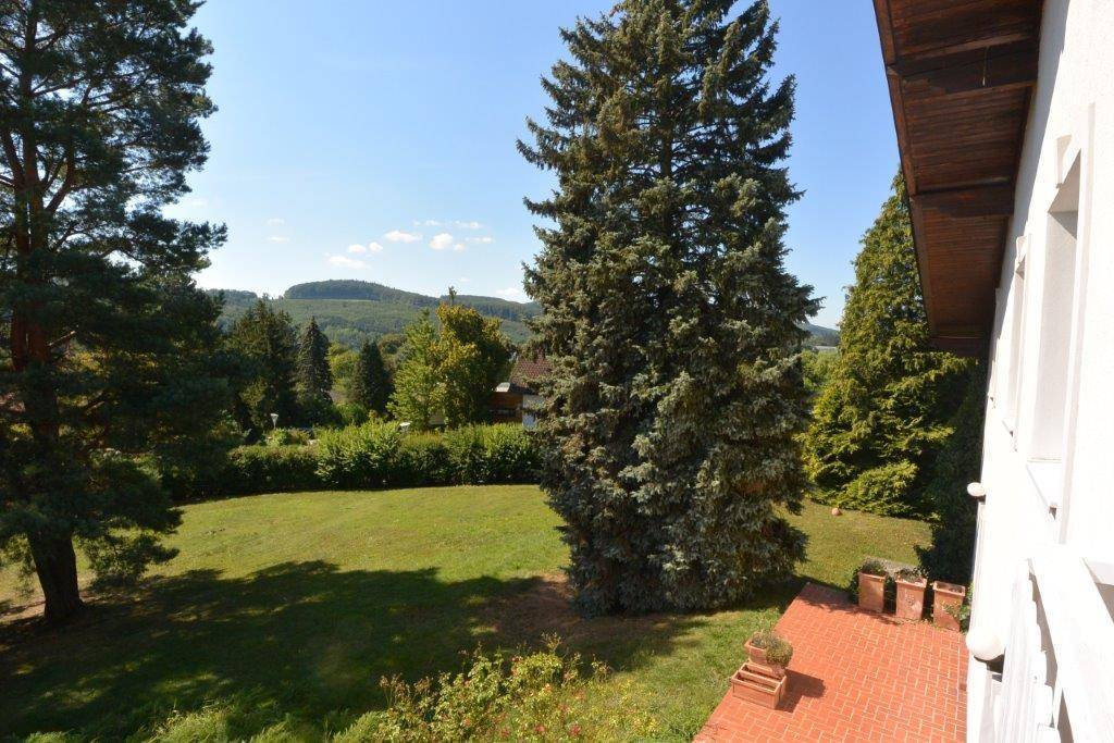 Malerischer Ausblick von der Terrasse auf die weite, grüne Hügellandschaft und hohe Bäume.