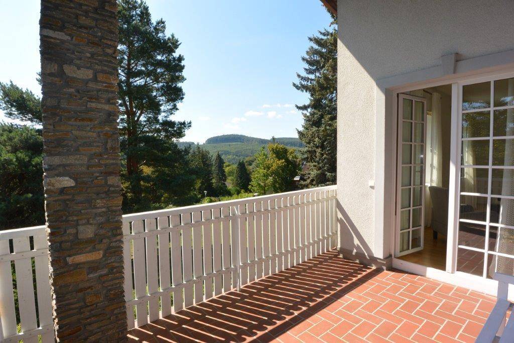Heller Balkon mit weißem Geländer und weitem Blick über die grüne Landschaft.