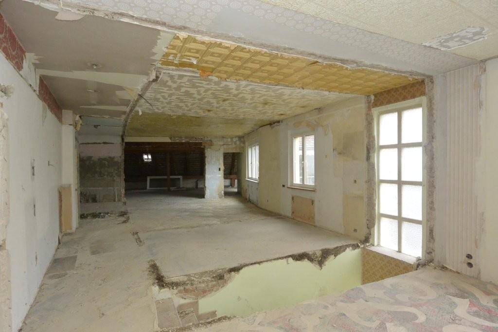 Großer Raum im Umbau mit sichtbaren Deckenstrukturen und Fenstern, die viel Licht hereinlassen.