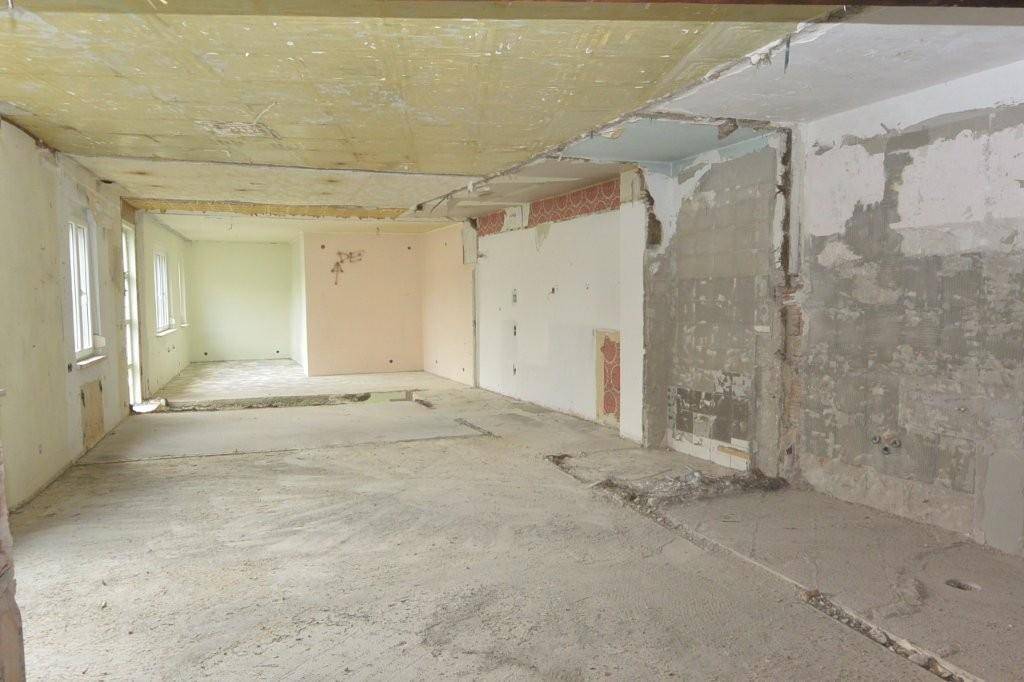 Innenraum im Rohbau mit freigelegten Wänden und Decken, bereit für die Neugestaltung des Bodens.