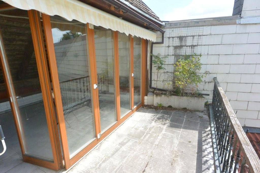 Große verglaste Front führt zu einer sonnigen Terrasse mit Markise und Metallgeländer.