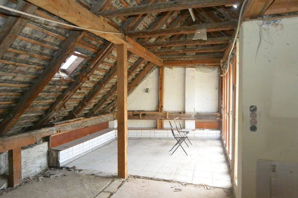 Dachboden im Rohzustand mit sichtbarer Dachkonstruktion, Dachfenster und teilweise gefliestem Boden.