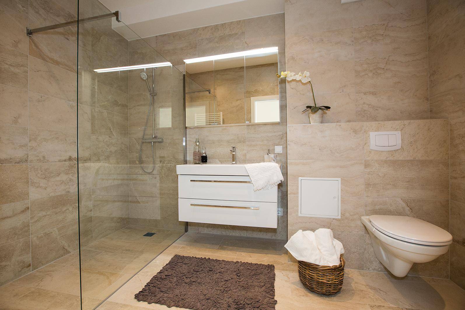 Modernes Badezimmer mit beigen Fliesen, ebenerdiger Dusche und wandhängendem WC.