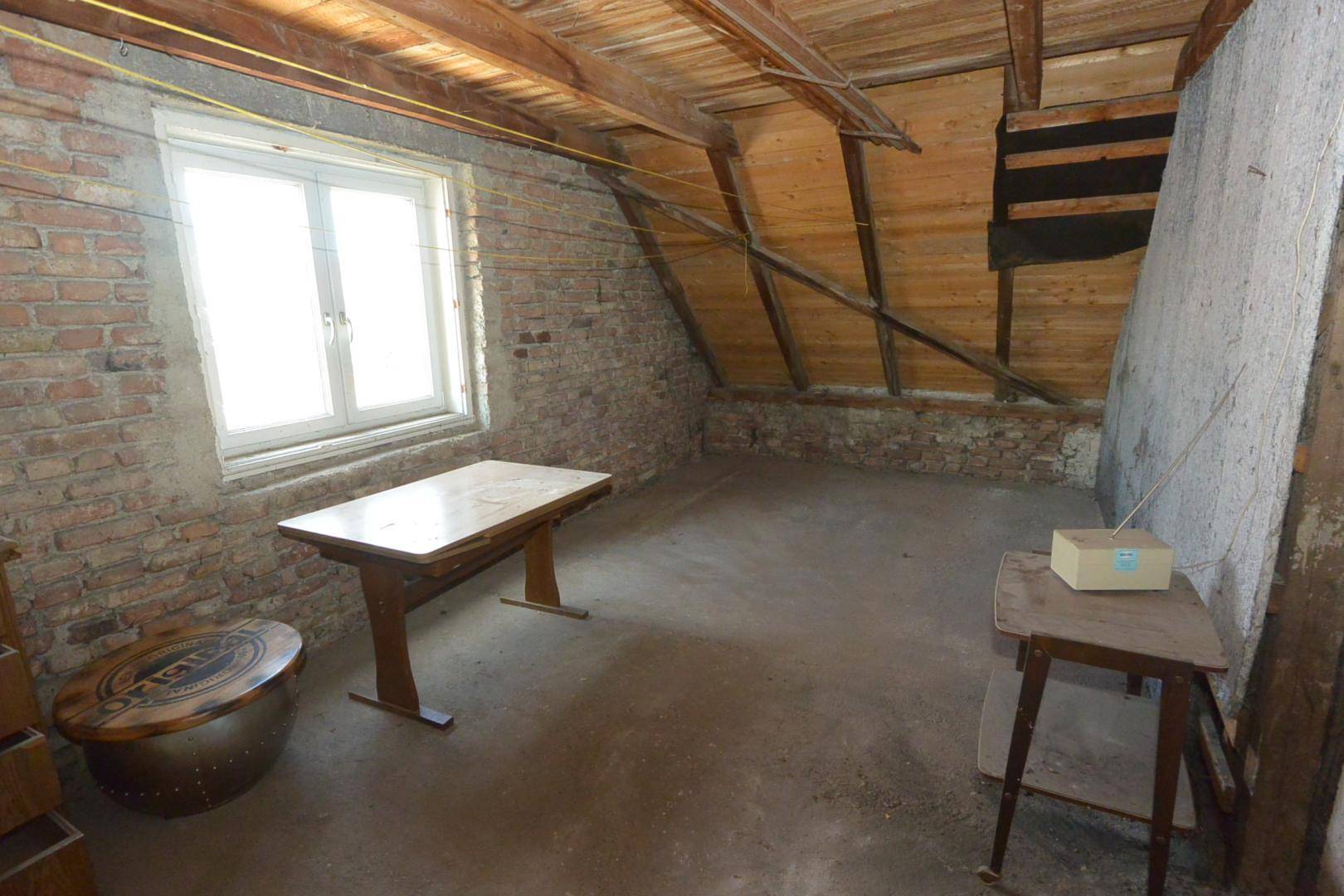 Dachbodenraum mit freiliegenden Holzbalken, Ziegelwänden und einem Fenster.