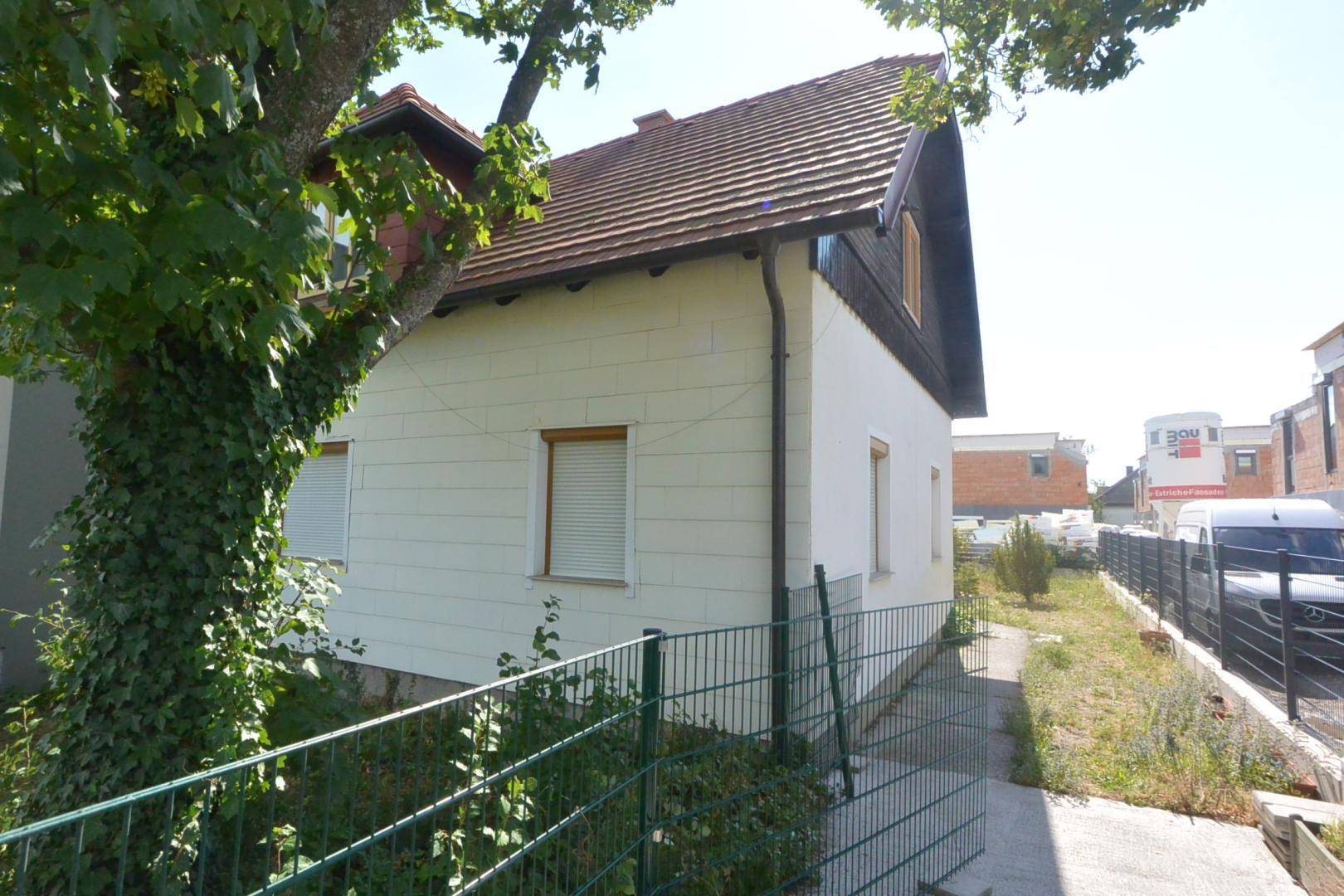 Seitenansicht des Hauses mit weißer Fassade, braunem Dach und einem grünen Zaun.