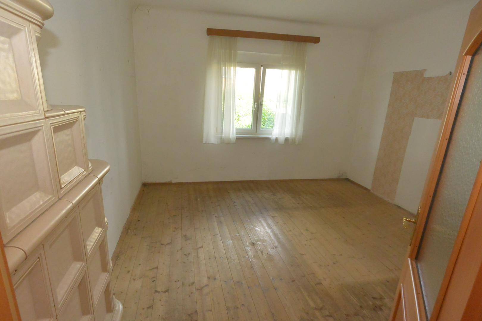 Leeres Schlafzimmer mit Holzdielenboden, weiß gestrichenen Wänden und einem Fenster.