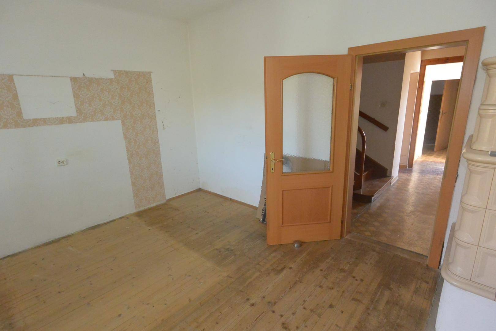Leeres Zimmer mit Holzdielenboden und einer Holztür, die zum Flur führt.