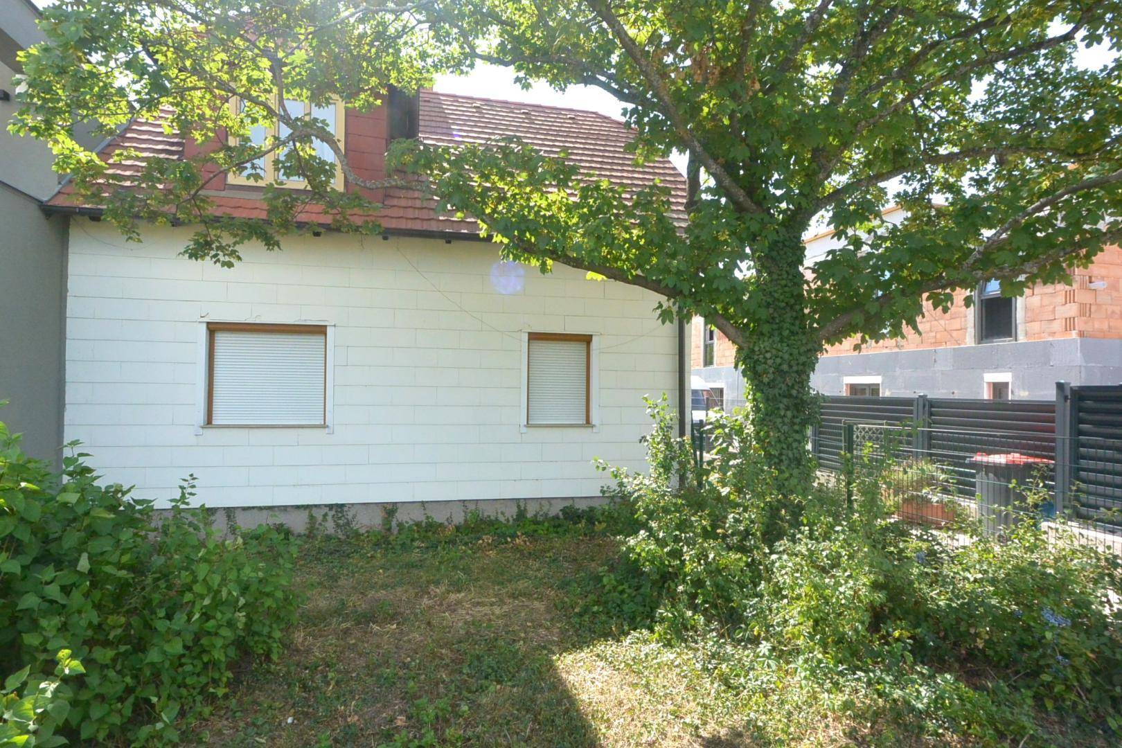 Seitenansicht des Hauses mit einem großen Baum im Vordergrund und einem Zaun.