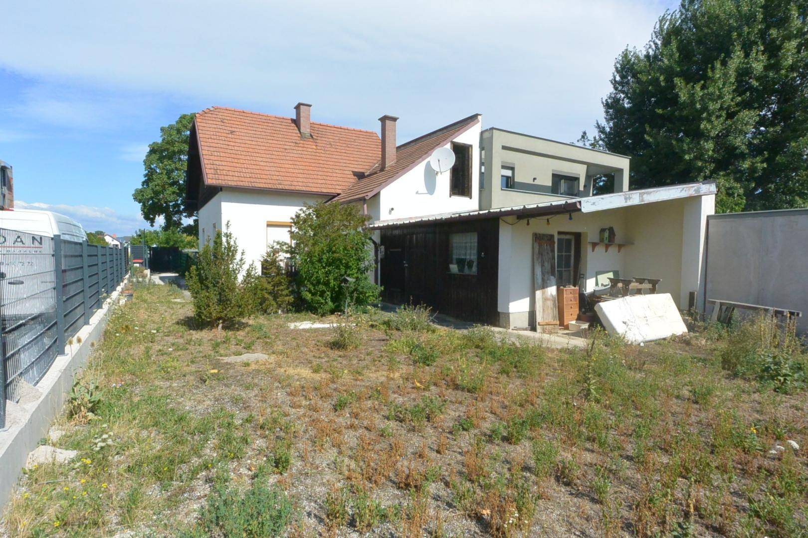 Rückansicht des Hauses mit einem ungepflegten Gartenbereich und angrenzendem Anbau.