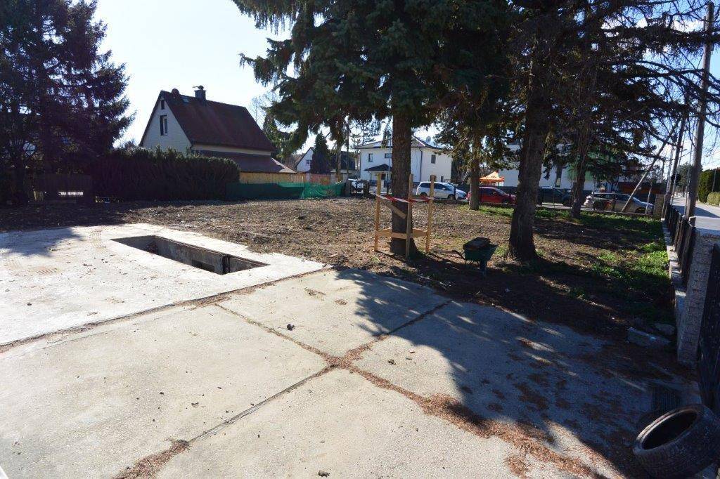 Grundstück mit einer Betonfläche und einer Grube, umgeben von Bäumen und Häusern.