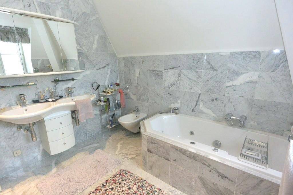 Luxuriöses Badezimmer mit Marmorfliesen, Doppelwaschbecken, Bidet und Eckbadewanne mit Whirlpoolfunktion.