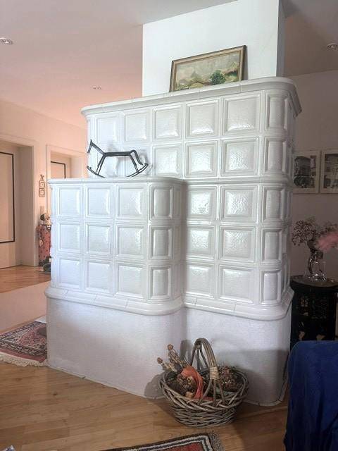 Detailansicht eines eleganten weißen Kachelofens mit traditionellem Design, umgeben von einem bunten Teppich.
