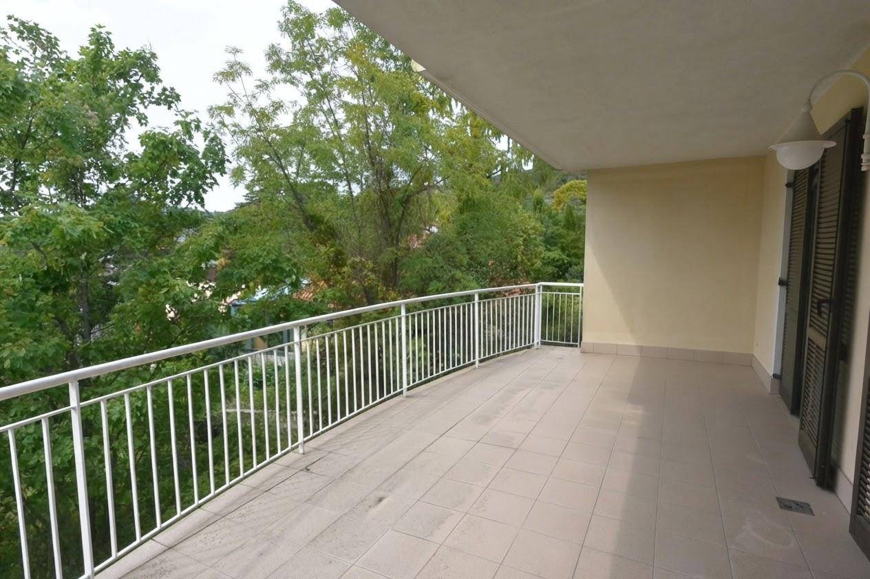 Leerer Balkon mit Fliesenboden und weißem Geländer, bietet viel Platz und einen schönen Ausblick ins Grüne.
