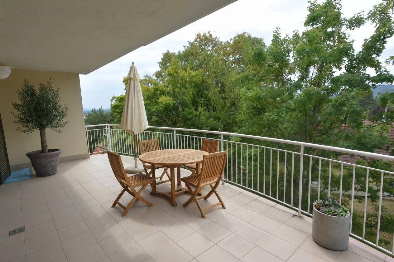 Großer Balkon mit Esstisch, Stühlen und Sonnenschirm, ideal für Mahlzeiten im Freien mit Blick ins Grüne.