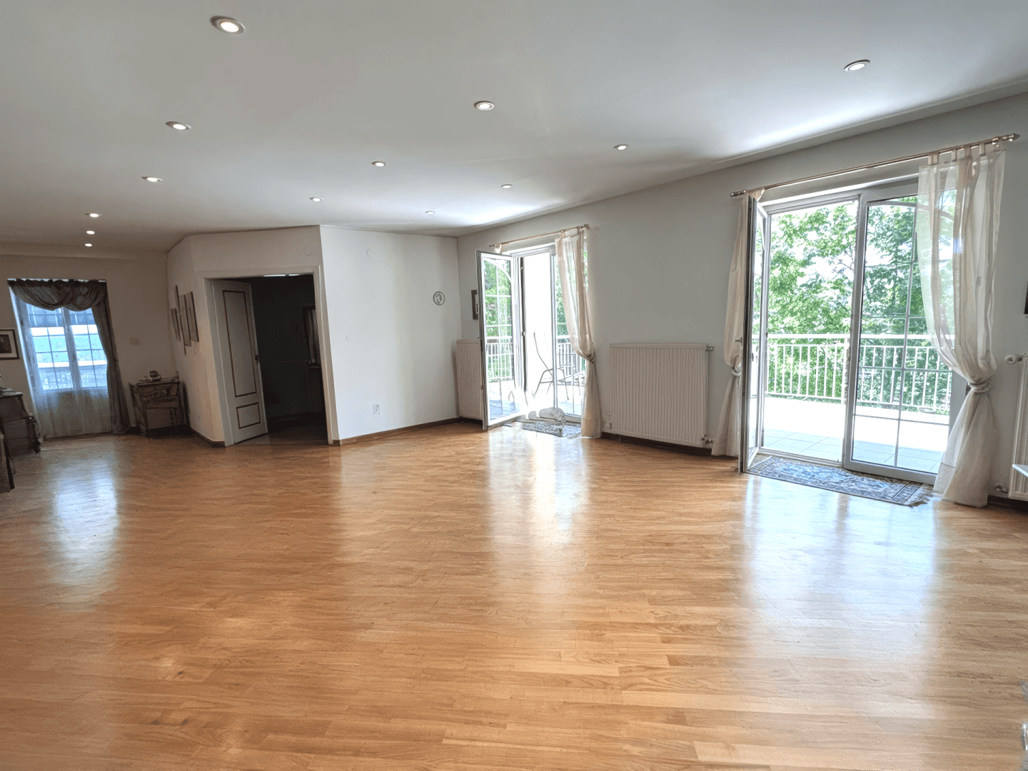 Geräumiges, leeres Wohnzimmer mit hellem Parkettboden und zwei Balkonzugängen, bietet viel Gestaltungspotenzial.