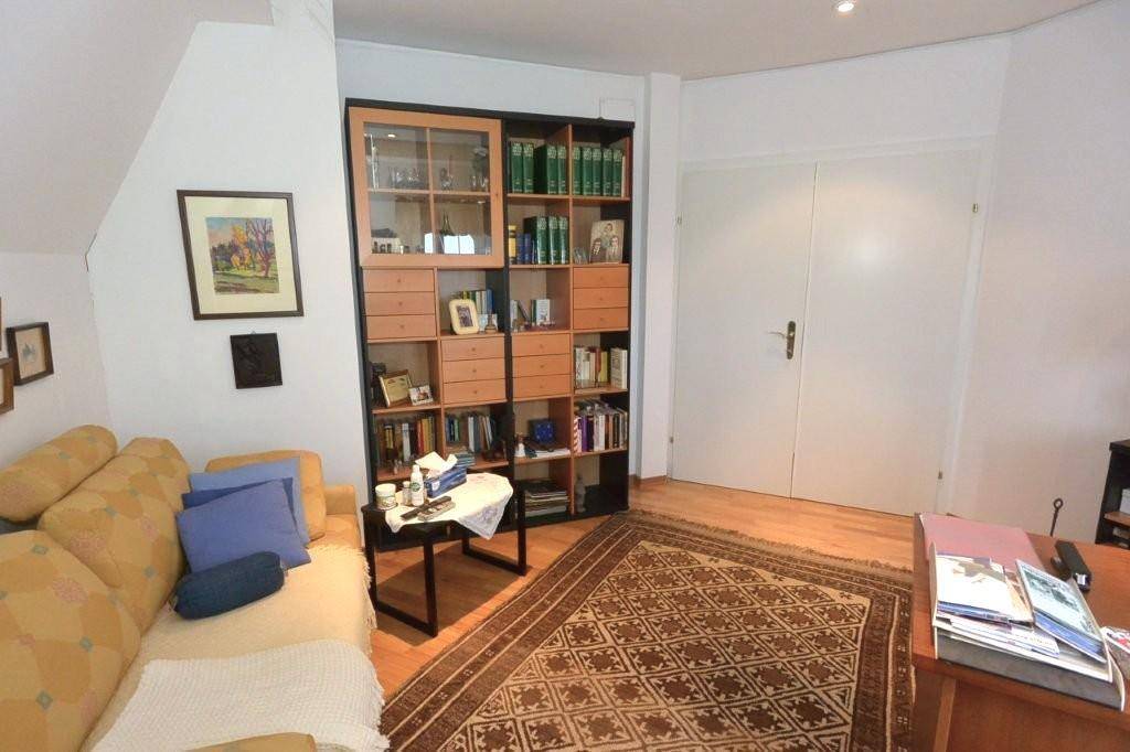 Arbeitszimmer mit Sofa, großem Bücherregal und hellem Parkettboden, bietet Stauraum und eine Leseecke.
