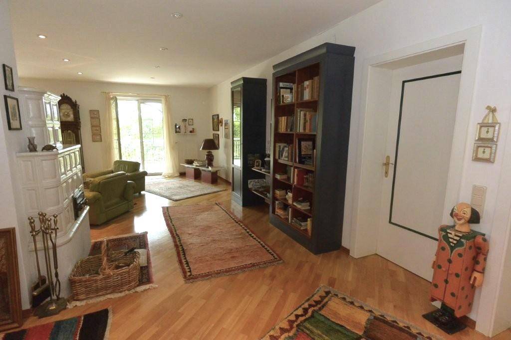 Gemütliches Wohnzimmer mit hellem Parkettboden, traditionellem Kachelofen und Bücherregalen, strahlt Wärme aus.