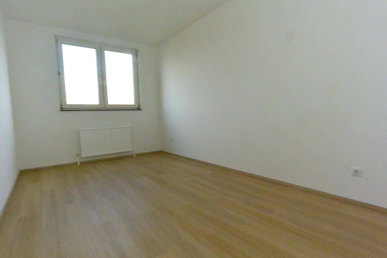 Leeres Schlafzimmer mit hellem Laminatboden, weißen Wänden und einem Fenster.