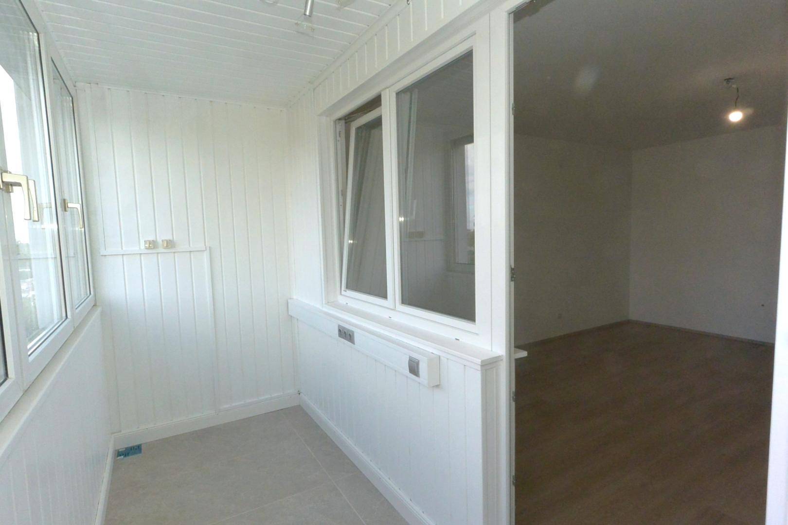 Heller, verglaster Balkon mit weißen Paneelen und Fliesenboden, mit Zugang zum Innenraum.