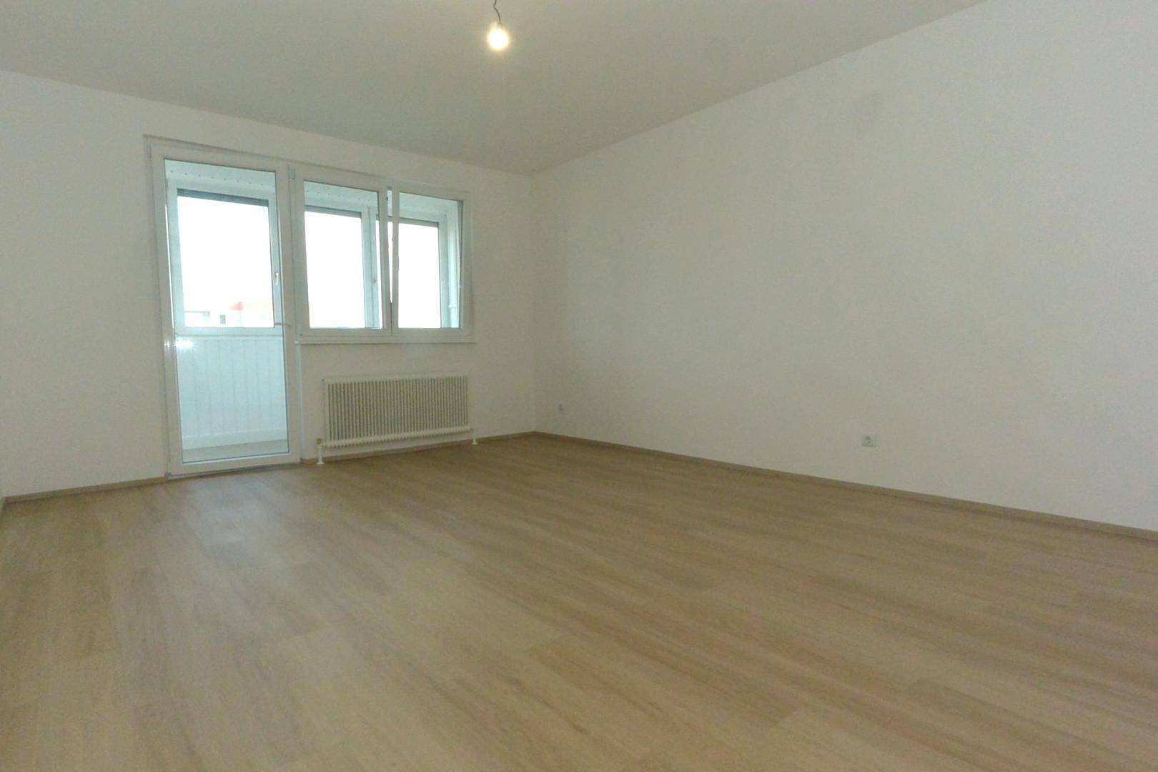Unmöblierter Raum mit Laminatboden, weißen Wänden und Fensterfront zum Balkon.