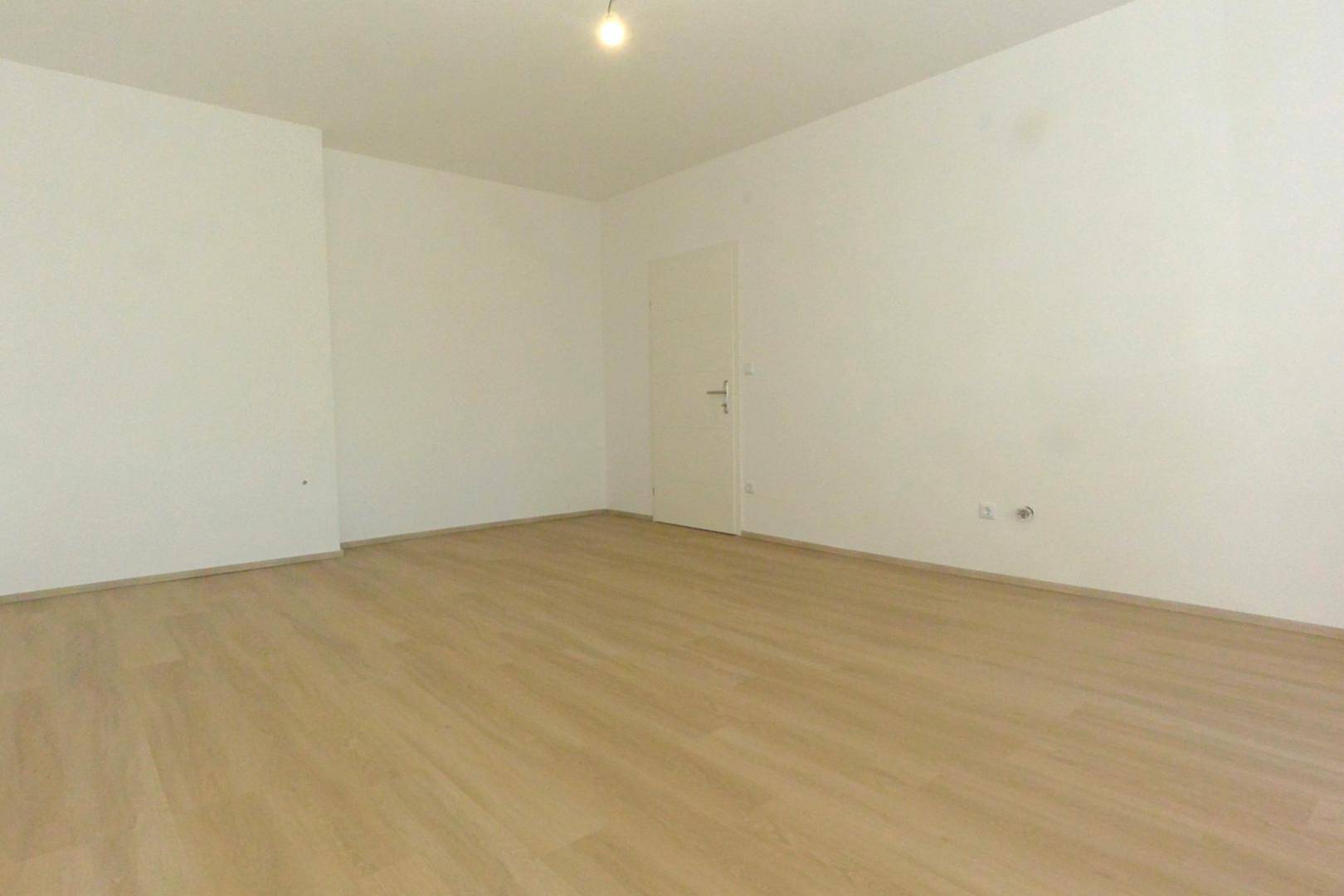 Leerer Raum mit hellem Laminatboden und weißen Wänden, bereit zur individuellen Gestaltung.