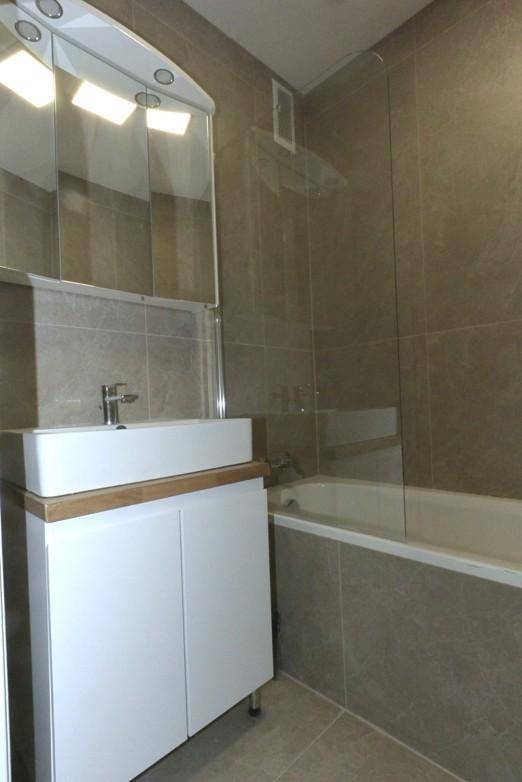 Modernes Badezimmer mit Waschtisch, Spiegelschrank und Badewanne mit Duschwand.