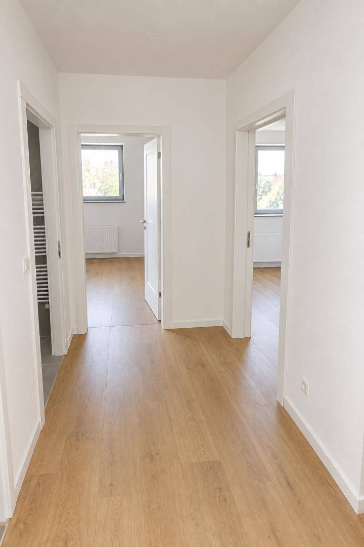 Heller Flur mit Laminatboden und weißen Wänden, der zu verschiedenen Zimmern führt.