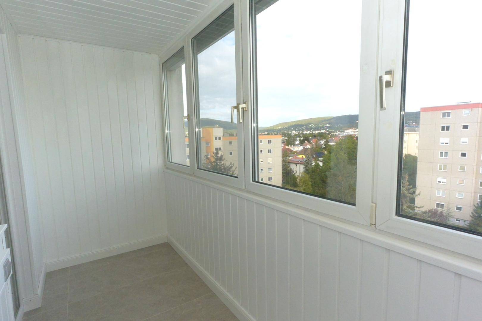Verglaster Balkon mit Stadtblick und grünen Hügeln im Hintergrund, hell und freundlich.