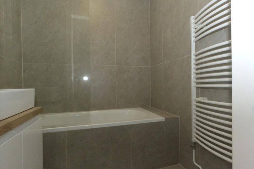 Badezimmer mit Badewanne und beheiztem Handtuchhalter, komplett gefliest.