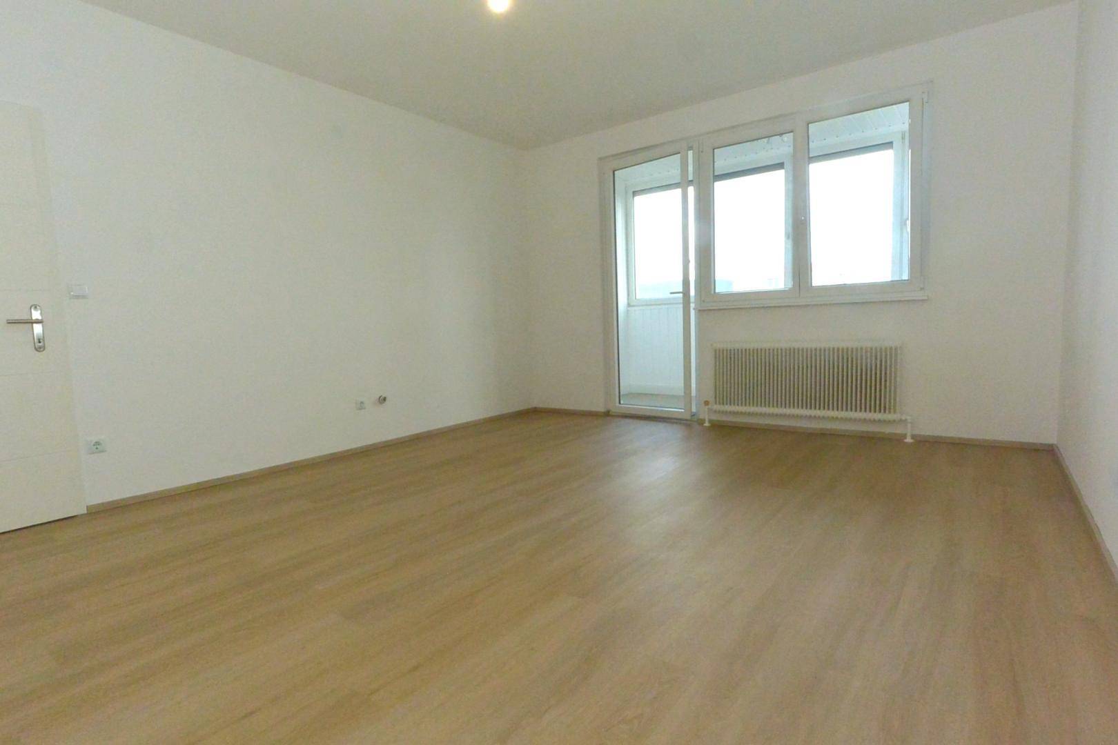 Helles, unmöbliertes Zimmer mit Laminatboden, weißen Wänden und Balkonzugang.