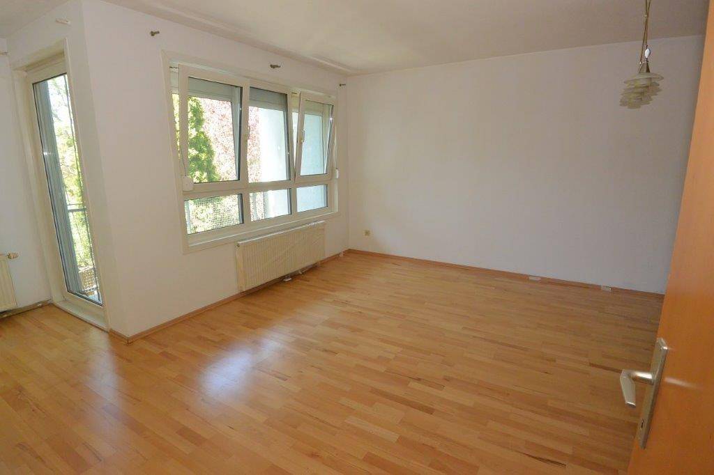 Geräumiges, leeres Zimmer mit Parkettboden, großen Fenstern und direktem Zugang zu einem Balkon.