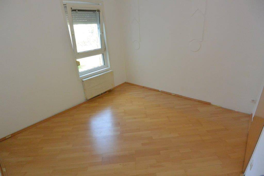 Helles, leeres Zimmer mit Parkettboden und einem Fenster, das für natürliche Belichtung sorgt.