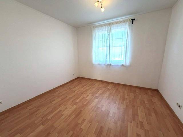 Helles Schlafzimmer mit Laminatboden und einem Fenster, bereit zur individuellen Gestaltung.