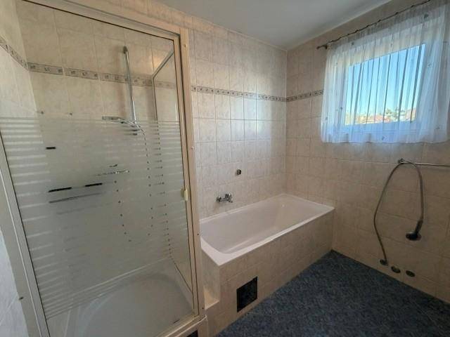 Funktionales Badezimmer mit Badewanne, Duschkabine und Fenster, hell gefliest.