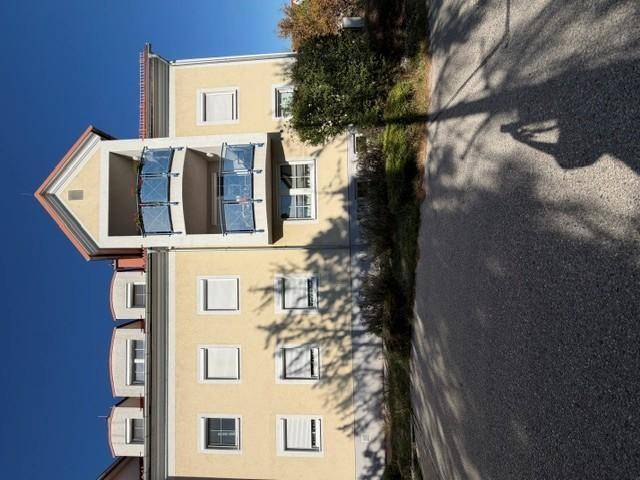 Mehrfamilienhaus mit heller Fassade, zahlreichen Fenstern und Balkonen unter blauem Himmel.