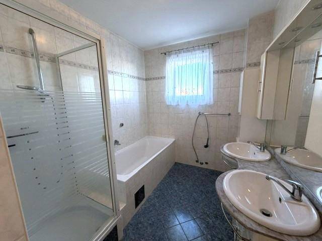 Gefliestes Badezimmer mit Doppelwaschbecken, Badewanne, Duschkabine und Fenster.